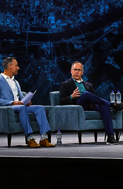 Dois homens falando no palco durante uma discussão em painel